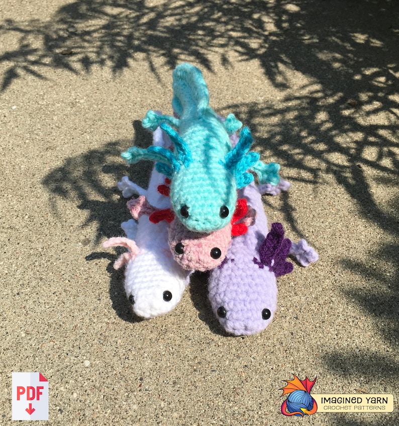 May include: Four crocheted axolotl plushies stacked on top of each other. The top axolotl is turquoise, the next is pink, the next is white, and the bottom axolotl is purple. The axolotls are all facing the camera.