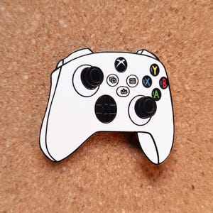 Op de afbeelding: Witte Xbox-controller met zwarte accenten en gekleurde knoppen. De controller heeft een D-pad, twee joysticks en knoppen met letters en symbolen. Een klassiek gaming-accessoire.