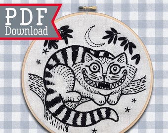 Puede incluir: Patrón de bordado en blanco y negro del Gato de Cheshire de Alicia en el País de las Maravillas, con una luna creciente y estrellas en el fondo. El patrón está en un aro y dice "Kindred Spirit Art Studio" en la parte inferior.