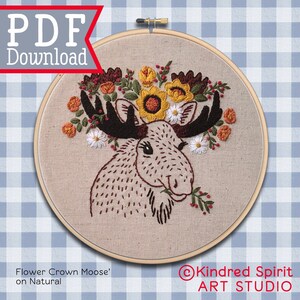 May include: Embroidered hoop art featuring a moose with a flower crown. The moose is brown with a white face and is surrounded by a variety of flowers in shades of yellow, orange, and white. The background is a blue and white checkered pattern. The text "Flower Crown Moose' on Natural" is at the bottom left of the image. The text "@Kindred Spirit ART STUDIO" is at the bottom right of the image.