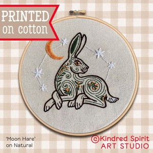 May include: Embroidered hoop art featuring a stylized green hare with a crescent moon and stars. The text "Moon Hare" and "on Natural" is printed below the hoop. The text "Kindred Spirit ART STUDIO" is printed below the hoop.