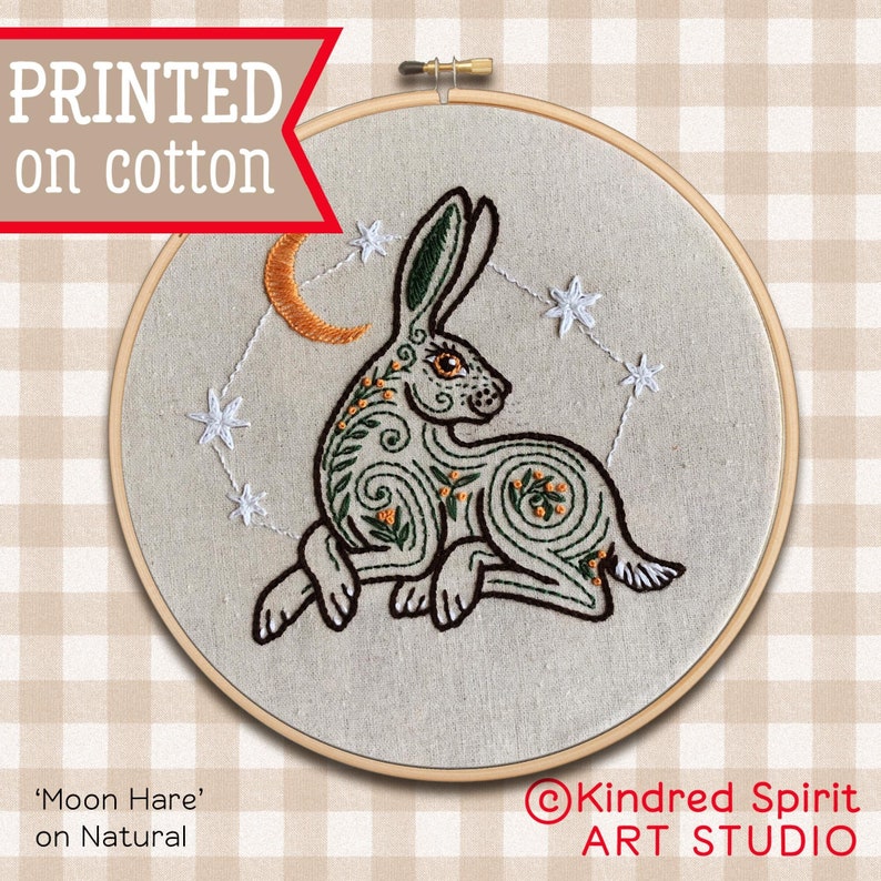 May include: Embroidered hoop art featuring a stylized green hare with a crescent moon and stars. The text "Moon Hare" and "on Natural" is printed below the hoop. The text "Kindred Spirit ART STUDIO" is printed below the hoop.