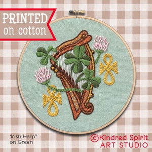 Puede incluir: Un aro de bordado de tela verde con un marco de madera marrón. El diseño presenta un arpa celta con tréboles y un nudo celta. El texto "Irish Harp" y "on Green" está impreso debajo del aro. El texto "Kindred Spirit ART STUDIO" está impreso debajo del aro.