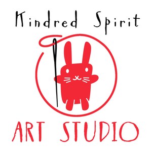 May include: A red circle with a red bunny holding a black needle and thread. The text "Kindred Spirit Art Studio" is written in black above and below the circle.