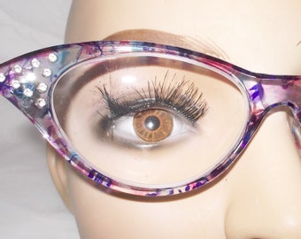 Puede incluir: Gafas de ojo de gato con un patrón floral morado, rosa y azul. Las gafas tienen lentes transparentes y diamantes de imitación en el borde superior.
