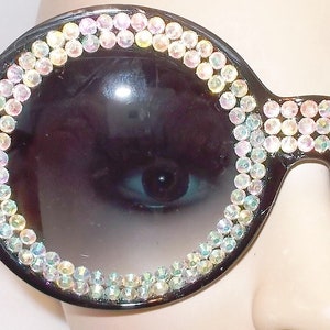 May include: Black round sunglasses with a thick frame and iridescent rhinestones around the lenses.