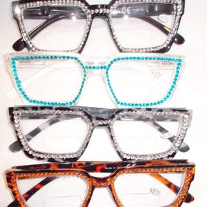 May include: Four pairs of reading glasses with decorative rhinestone accents. The frames are black, white, and tortoiseshell, with clear lenses. Each pair has a different color of rhinestones, including clear and turquoise.