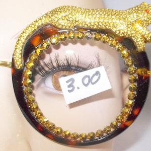May include: Tortoise shell round frame sunglasses with gold rhinestones and a gold jeweled animal design on the side. The price tag reads "3.00".