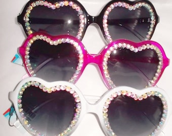 May include: Heart-shaped sunglasses in black, hot pink, and white. Each pair features a rhinestone-studded frame and dark lenses. A fun and fashionable accessory for any occasion.