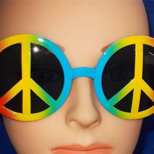 May include: Round, colorful sunglasses with a peace sign design. The lenses are black and the frame is a rainbow of colors, including red, orange, yellow, green, blue, and purple.
