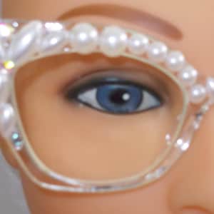 Puede incluir: Gafas transparentes de ojo de gato con un adorno de perlas y pedrería alrededor del marco.