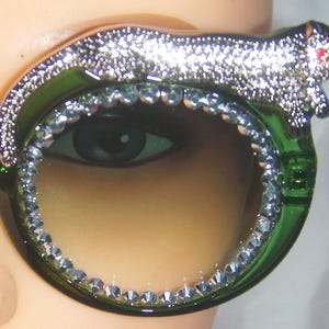 May include: Green and silver sunglasses with a rhinestone trim and a decorative animal design on the frame.