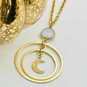 May include: Gold necklace with a moon charm and a white moonstone pendant. The necklace features two interlocking circles.