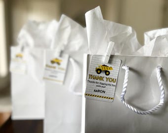 May include: White gift bags with tissue paper and a yellow and black construction truck thank you tag that says "Thank You Thanks for digging the fun with me! AARON".