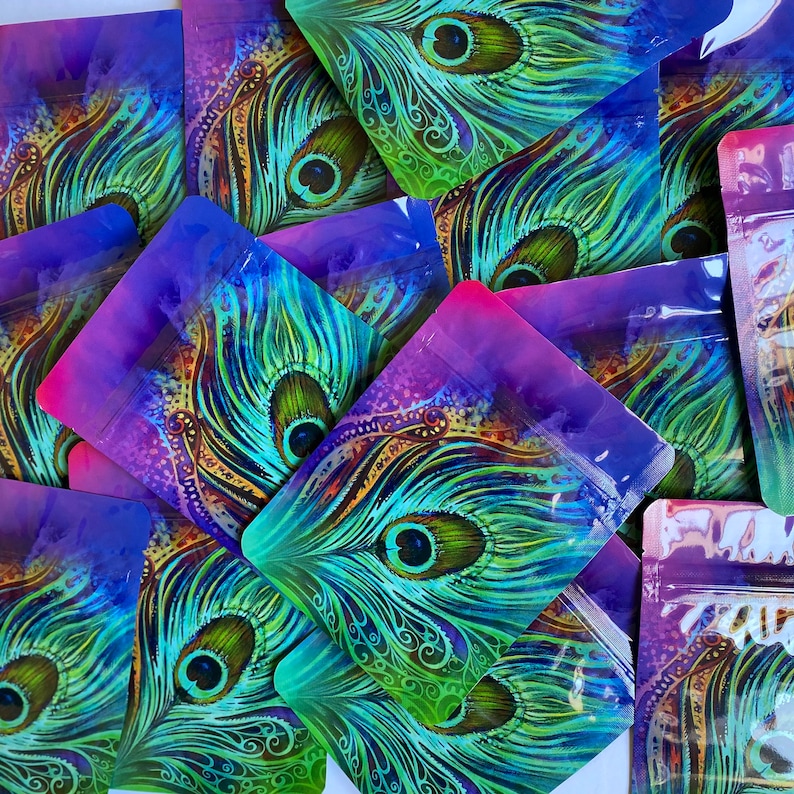 May include: A collection of colorful, iridescent, resealable pouches with a peacock feather design. The pouches are made of a clear, plastic-like material and have a purple, pink, and blue gradient.