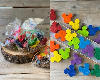 May include: The image showcases two distinct sets of colorful items. On the left, small, wrapped bundles of crayons are tied with various colored ribbons. On the right, a collection of Mickey Mouse-shaped crayons in a variety of colors are arranged in a box.