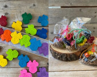 May include: A collection of colorful, shaped crayons in a wooden box and small cellophane bags. The crayons are in various colors, including red, orange, yellow, green, blue, and purple. The crayons are shaped like a cartoon character. The bags are tied with colorful twine.