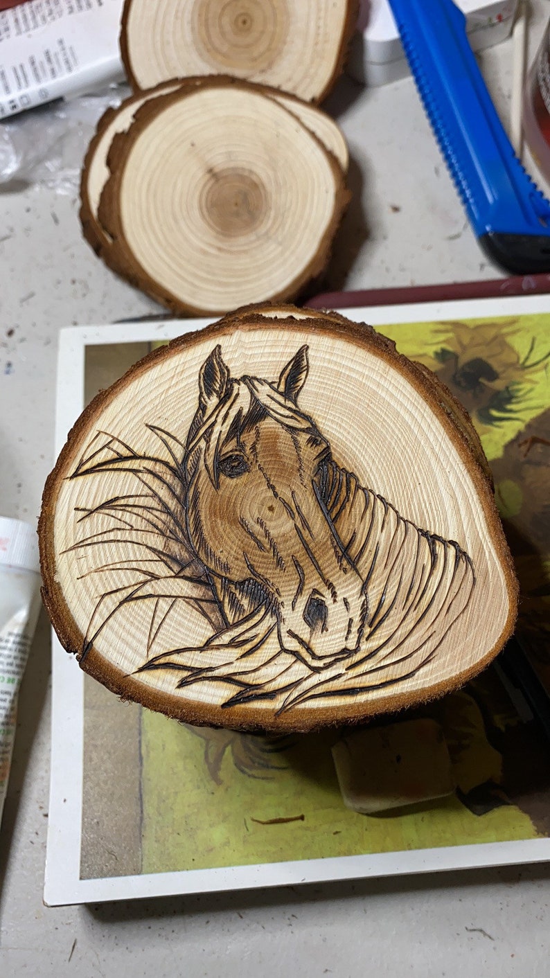 May include: A wood slice with a woodburned image of a horse's head. The horse is facing the viewer and has a brown coat. The wood slice is a light brown color and has a natural wood grain.