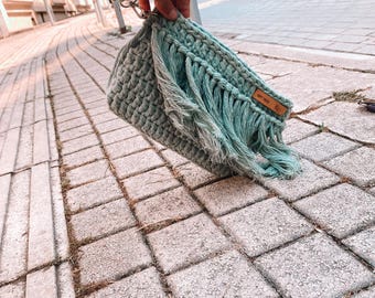 May include: A light green crocheted bag with fringe detailing and a brown leather tag that says "Soft Touch".