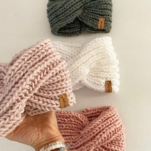 May include: Three knitted headbands in different colours: olive green, light pink, and a darker pink. Each headband has a brown leather tag with the text "Soft Touc" on it.