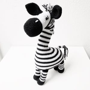 May include: A black and white striped crocheted zebra toy. The zebra has a black nose and black ears.