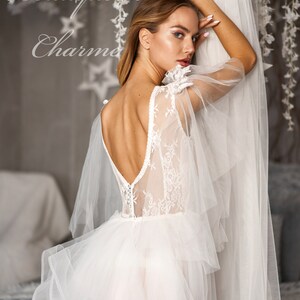 May include: A white wedding dress with a lace bodice and tulle skirt. The dress has a low back and a flowing skirt. The dress is being worn by a model in a studio setting.