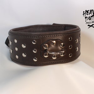 Könnte beinhalten: Ein dunkelbraunes Lederhalsband für Hunde mit silberfarbenen Nieten und einem Metall-D-Ring. Der Kragen trägt den Text "HEAVY DUTY COLLARS" in schwarzer, handschriftlicher Schrift.