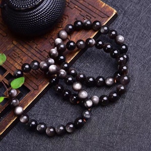 The natural silver obsidian round bead bracelet is essential for attracting wealth, good luck, and warding off evil spirits