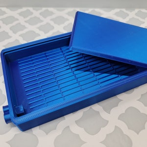 Puede incluir: Una caja de pl&aacute;stico azul con tapa. La caja tiene un patr&oacute;n de rejilla en el interior.