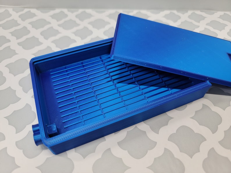 Puede incluir: Una caja de pl&aacute;stico azul con tapa. La caja tiene un patr&oacute;n de rejilla en el interior.