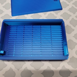 Puede incluir: Una caja de almacenamiento de pl&aacute;stico azul con un interior enrejillado. La caja tiene una tapa que no est&aacute; unida.