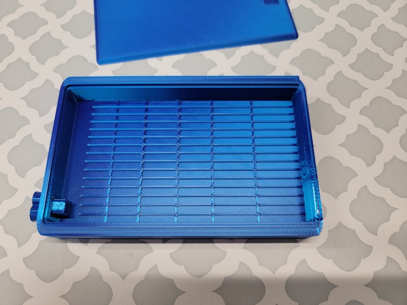 Puede incluir: Una caja de almacenamiento de pl&aacute;stico azul con un interior enrejillado. La caja tiene una tapa que no est&aacute; unida.