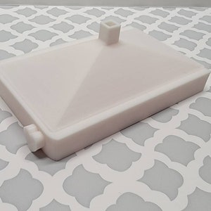 May include: White plastic rectangular base with a raised square platform in the center. The base has a small knob on the side.