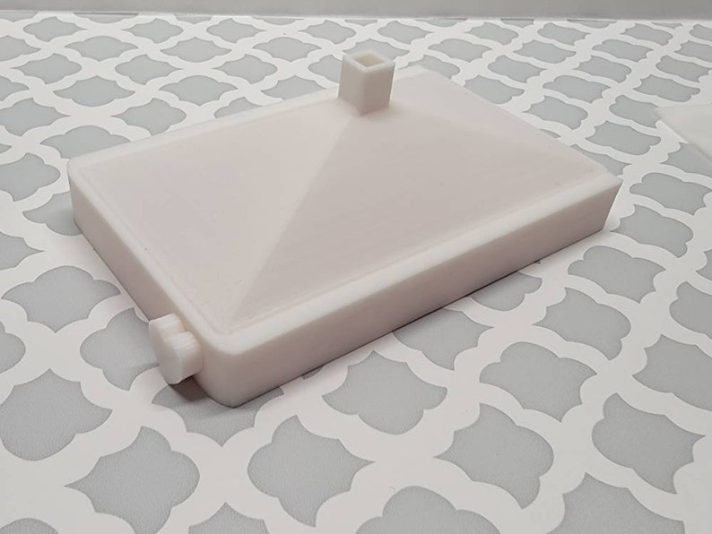 May include: White plastic rectangular base with a raised square platform in the center. The base has a small knob on the side.