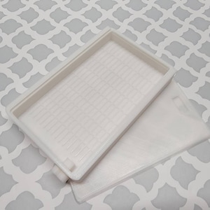May include: White plastic storage box with a textured lid and a smooth bottom. The box is open and the lid is laying on top of the box.