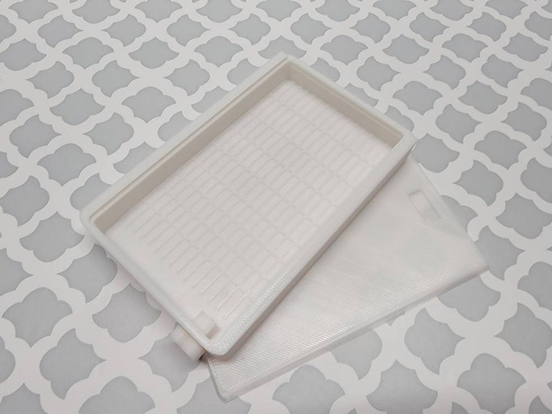 May include: White plastic storage box with a textured lid and a smooth bottom. The box is open and the lid is laying on top of the box.
