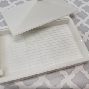 Puede incluir: Caja de almacenamiento de pl&aacute;stico blanco con tapa e interior enrejillado. La caja est&aacute; vac&iacute;a.