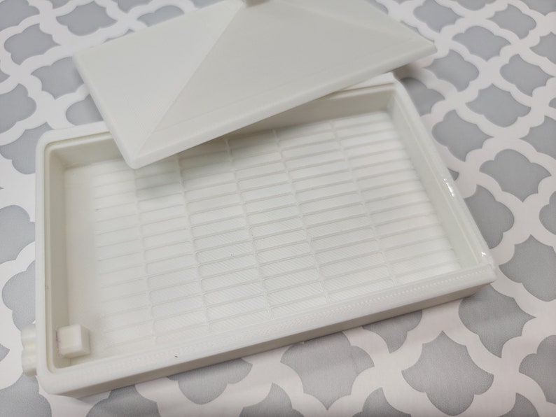 Puede incluir: Caja de almacenamiento de pl&aacute;stico blanco con tapa e interior enrejillado. La caja est&aacute; vac&iacute;a.