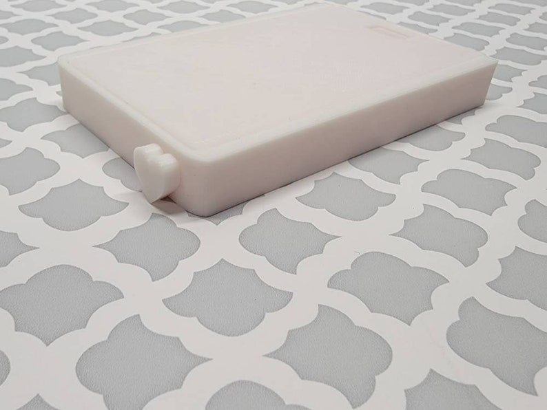 May include: A white plastic rectangular box with a small heart-shaped knob on the side.