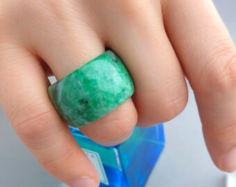 May include: A wide green jade ring with a smooth, polished surface. The ring is worn on a finger.