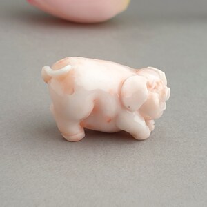 Peut inclure: Une petite figurine de cochon en corail rose. Le cochon est sculpt&eacute; en position debout, la t&ecirc;te tourn&eacute;e sur le c&ocirc;t&eacute;. La figurine est en corail lisse et poli.
