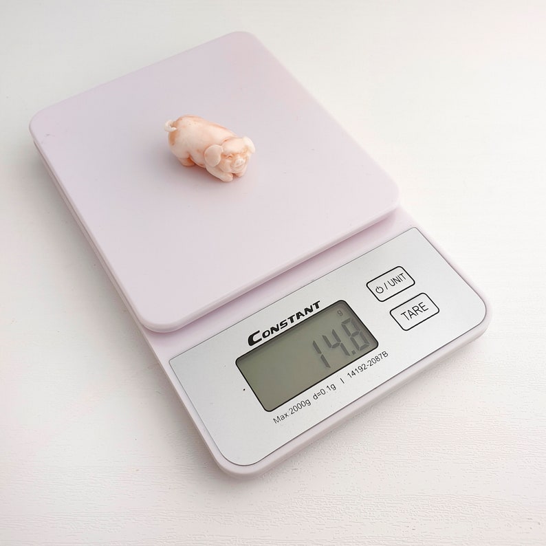 Peut inclure: Une figurine de cochon en corail rose sur une balance num&eacute;rique blanche. La balance affiche 14,8 grammes.