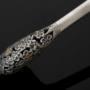 May include: A silver and gold-toned decorative handle with a floral design. The handle is intricately detailed with small flowers and leaves.