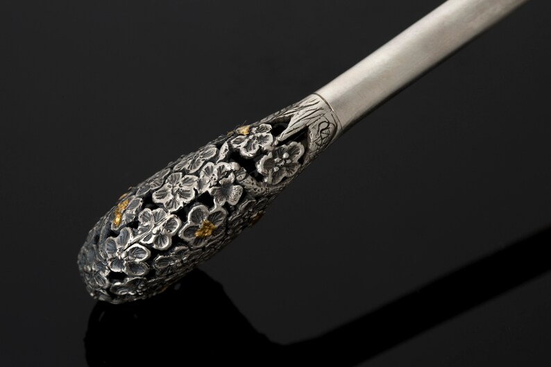 May include: A silver and gold-toned decorative handle with a floral design. The handle is intricately detailed with small flowers and leaves.