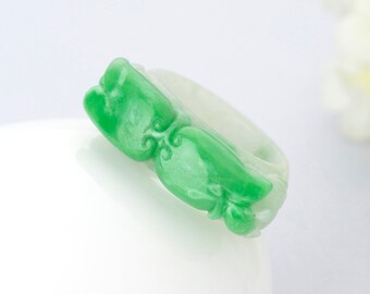 Könnte beinhalten: Ein grüner Jade-Ring mit einem geschnitzten Design aus zwei sich gegenüberstehenden Vögeln. Der Ring ist aus weißem Jade mit grünen Jade-Akzenten gefertigt.
