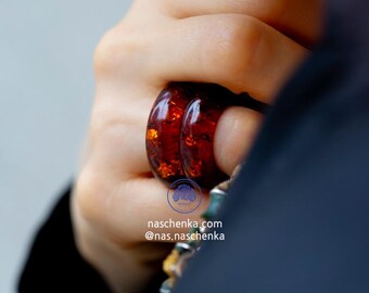 May include: A close-up of a person's hand wearing two amber rings. The rings are stacked on top of each other and are a deep orange color. The rings are made of natural amber and have a unique, organic shape. The text "naschenka.com @nas.naschenka" is visible in the image.