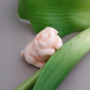 Peut inclure: Une petite figurine de cochon rose en corail sculpt&eacute;, pos&eacute;e sur une feuille verte.