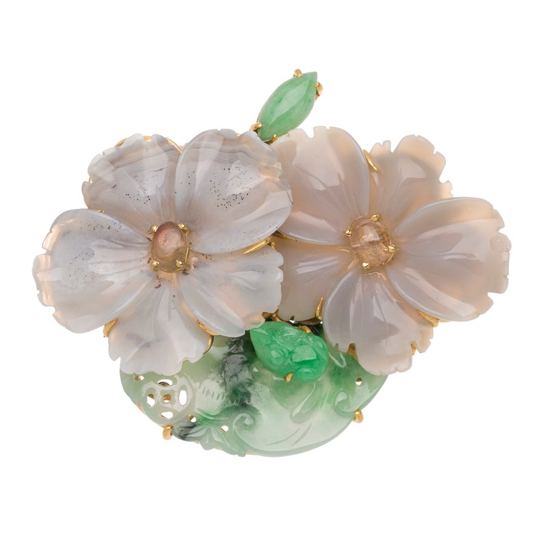 以下が含まれることがあります： 翡翠と瑪瑙で作られたブローチ。2つの花が彫刻されており、金色のアクセントが施されています。花はピンクがかった白で、繊細で複雑なデザインが施されています。葉は鮮やかな緑色です。