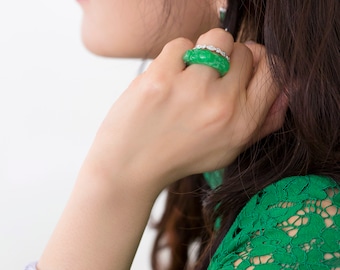 Könnte beinhalten: Eine Frau trägt ein grünes Spitzenkleid mit einem Jade-Armband am linken Handgelenk und einem Jade-Ring am rechten Ringfinger.