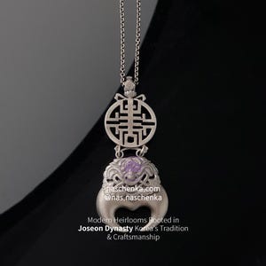 May include: A silver-toned pendant with a chain, featuring a circular design with a geometric pattern and a lower section with a purple gemstone. The pendant has a unique, ornate design, and the text "naschenka.com" is visible.
